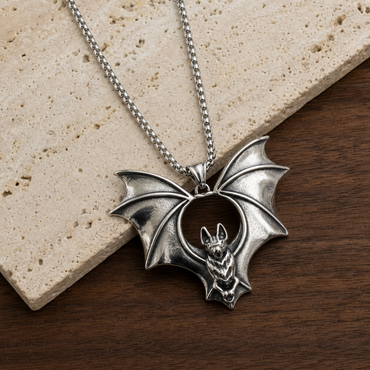 Silver flying bat pendant necklace photographed on travertine and walnut