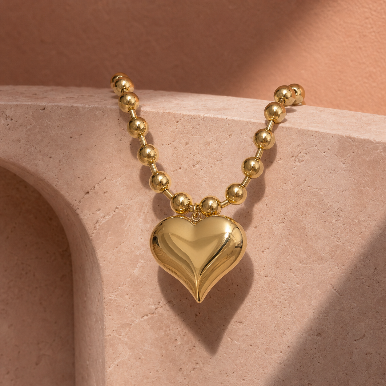 Polished gold heart and bead statement necklace on travertine