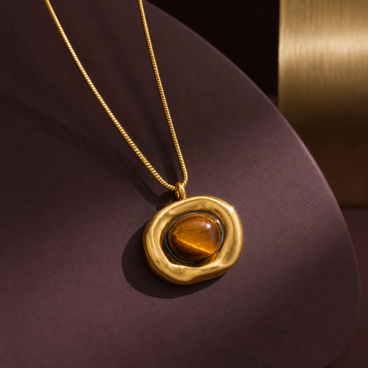 Irregular gold tiger-eye pendant necklace on an aubergine sculptural display