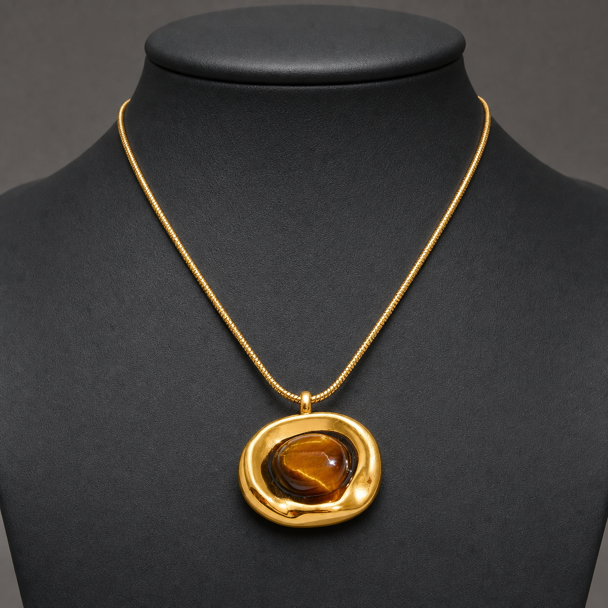 Irregular gold tiger-eye pendant necklace on charcoal jewelry bust