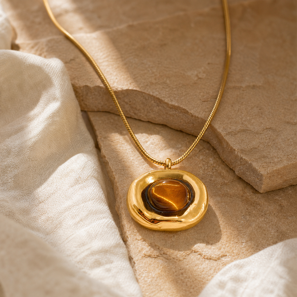 Irregular gold tiger-eye pendant necklace on sandstone and linen