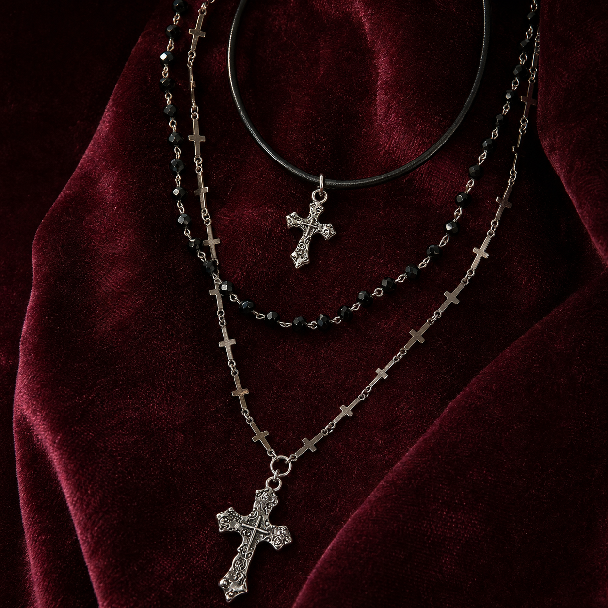 Layered Y2K cross and bead necklace styled on burgundy velvet