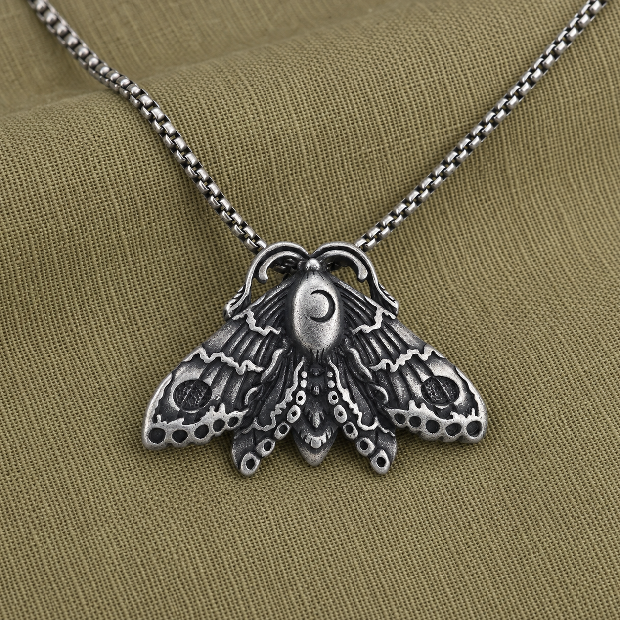 Gothic moon moth pendant necklace styled on olive linen