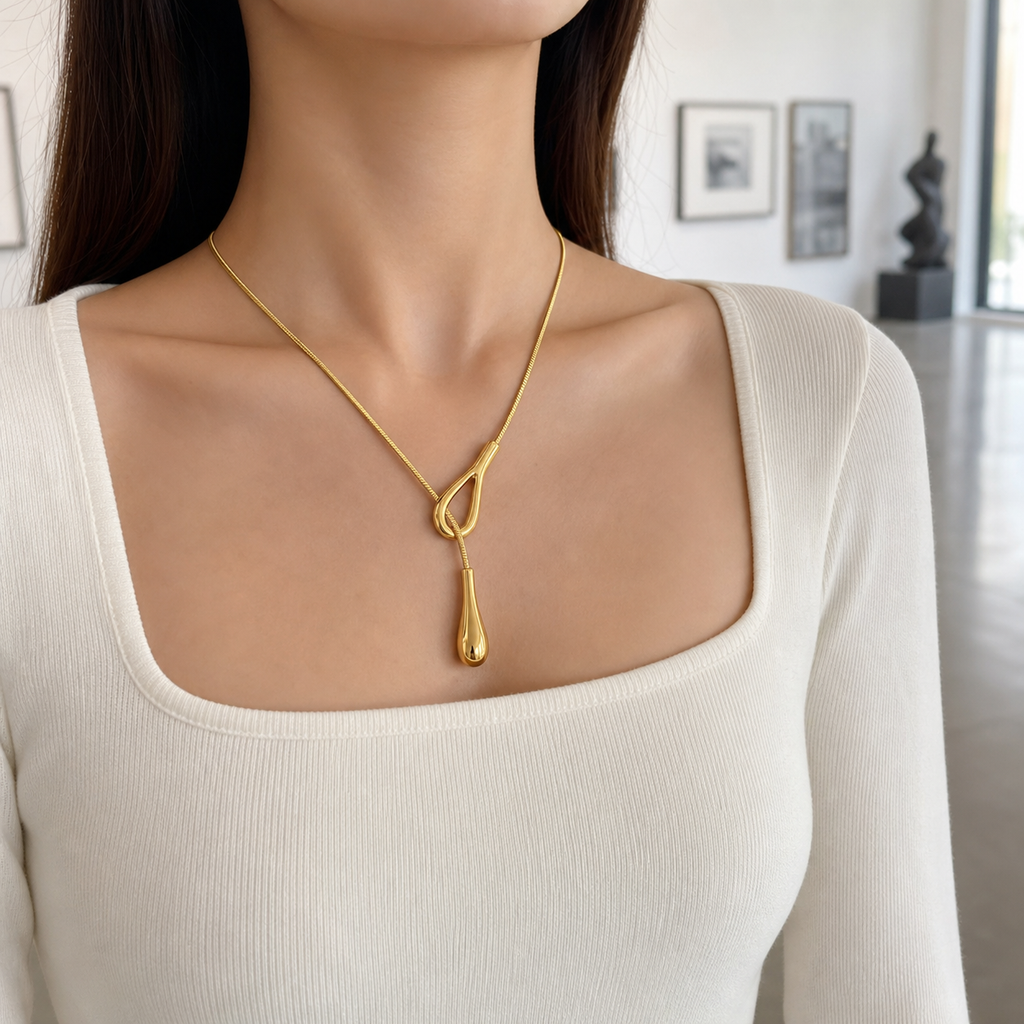 Sculptural gold waterdrop lariat necklace styled in a contemporary gallery