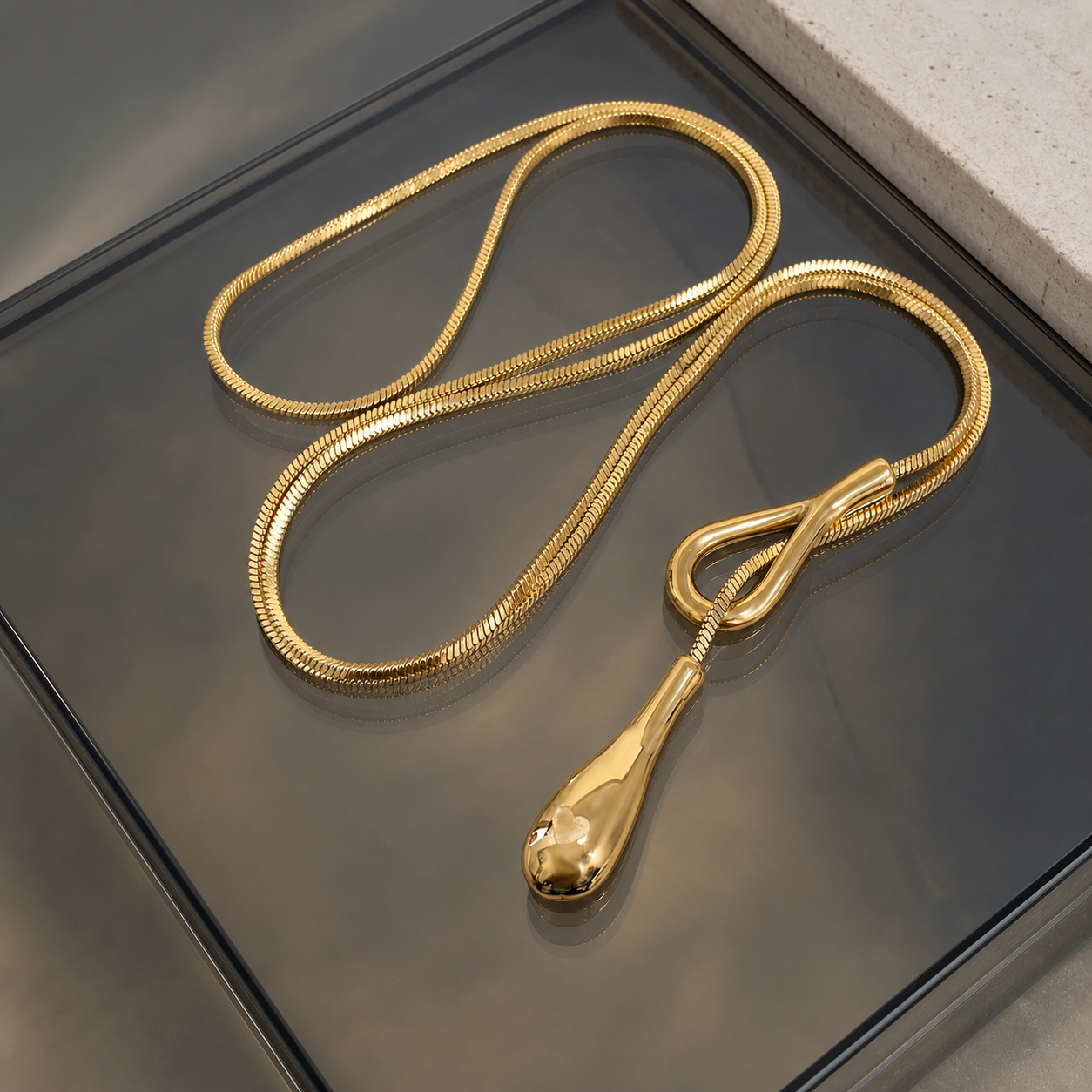 Sculptural gold waterdrop lariat necklace on smoked glass and limestone